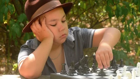 Young Boy Wearing Hat Thinking While Playing Chess Outdoors Video stock 343550233