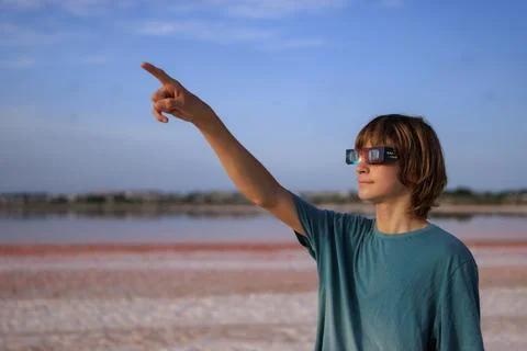 Young boy wearing solar eclipse glasses, pointing finger upwards, showing c.. Stock Photos