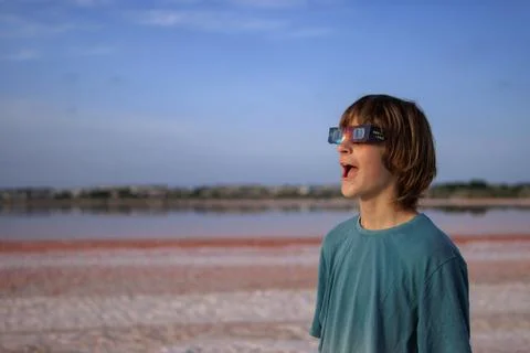 Young boy wearing solar eclipse glasses on a vibrant pink salt lake discove.. Stock Photos
