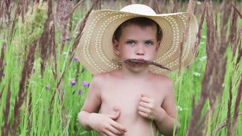 Young boy wears straw hat and playfully holds piece of grass. Stock Footage 287525436
