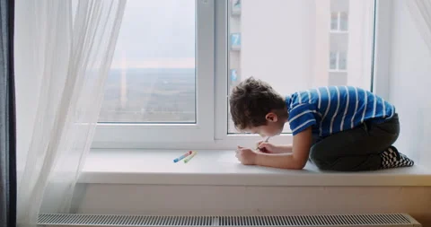 A young boy on a window sill expresses creativity through drawing Stock Footage 307297280