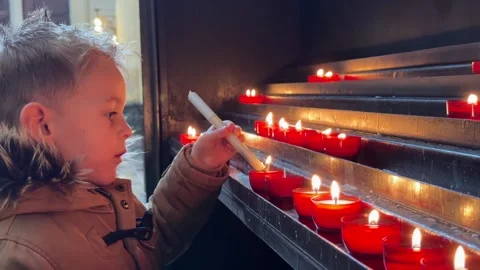 Young Boy In Winter Coat Lighting Candles Inside Church. close-up shot, side Stock Footage 335910276