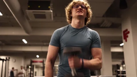 A young boy is working on his biceps in the gym, wearing a tight-fitting t-shirt Stock Footage 301677286