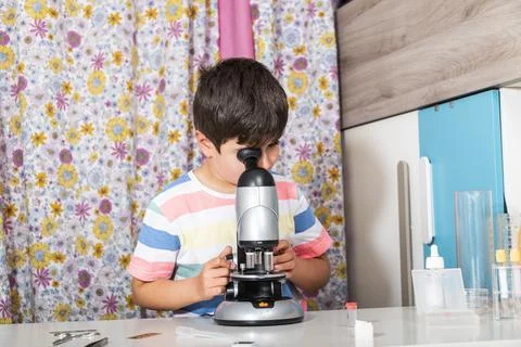 Young boy is working with the microscope and examines different things. Stock Photos
