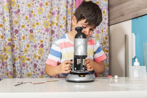 Young boy is working with the microscope and examines different things. Stock Photos