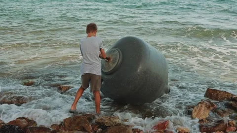 Young boy working to retrieve large, dark navigational buoy from shallow co.. Stock Footage 313555383