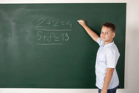 Young boy writing mathematical examples on the a school blackboard Stock Photos