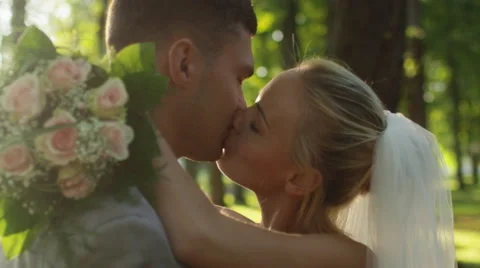 Young bride and groom are kissing in a sunny park Stock Footage