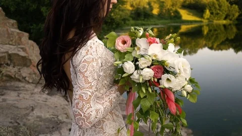 Young bride holding bouquet on the river bank, close-up Stock Footage
