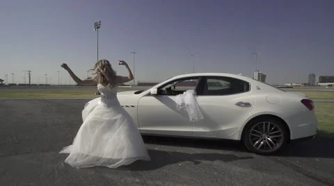 Young bride performs a crazy dance in front of a nice car 動画素材 61057332