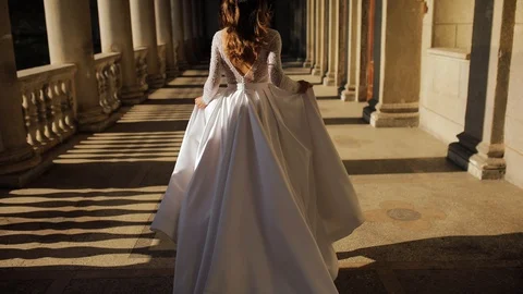 Young bride runs on the balcony among the columns on a Sunny day and her dress Vidéo 129781907
