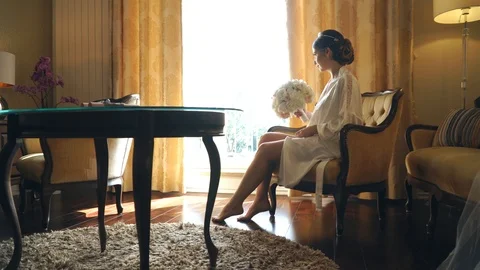 Young bride is sitting by the window in a luxury hotel with a bouquet of flowers 스톡 동영상 105683193