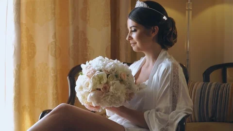 Young bride is sitting by the window in a luxury hotel with a bouquet of flowers 스톡 동영상 105683406