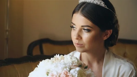 Young bride is sitting by the window in a luxury hotel with a bouquet of flowers 스톡 동영상 105683559