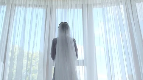 Young bride slowly opens the white tulle on the window on a summer morning Stock Footage 123426943