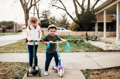 Young brother and sister riding scooters in front yard Stock Photos