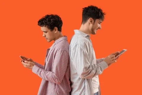 Young brothers using tablet computer and mobile phone on orange background Stock Photos