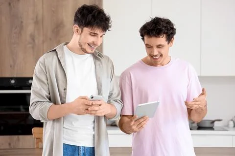 Young brothers using tablet computer and mobile phone in kitchen Stock Photos