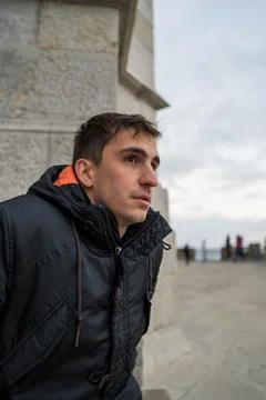Young brown haired man in front sitting on the street waiting for someone wit Stock Photos