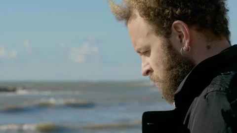 Young brown haired man looking down then up toward the sea 스톡 동영상 332418888