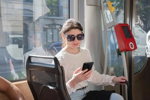 Young brunette browsing and typing messages on phone on way to work in tram Stock Photos