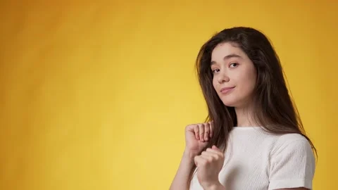 Young brunette dancing energetically and coquettishly against yellow background Stock Footage 247969750