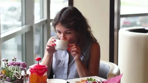 Young brunette is drinking tea in a cafe. woman eating breakfast in a cafe. 動画素材 138814262