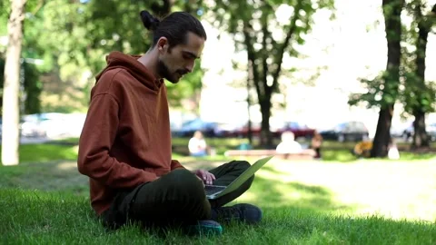 Young brunette freelancer man using modern laptop sitting in sunny green park en Video stock 139145383