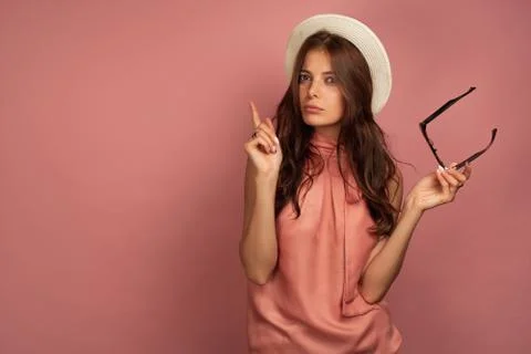 Young brunette in a hat thinks of something over pink background Stock Photos