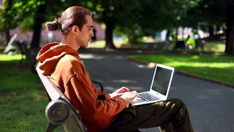 Young brunette hipster man using laptop in park outside in the city. Urban Vidéo 146844764