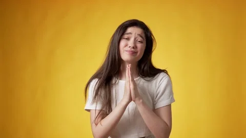 Young brunette joining palms in begging gesture against yellow background Stock Footage 247711119