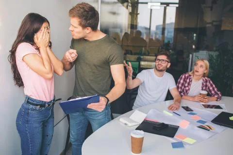Young brunette keep face closed with hands. She is afraid of guy standing Stock Photos