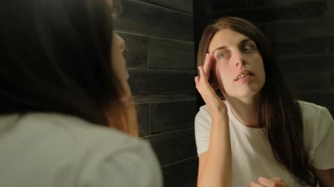 A young brunette looks at her reflection in front of a mirror. Hand touches. Stock Footage 138999788