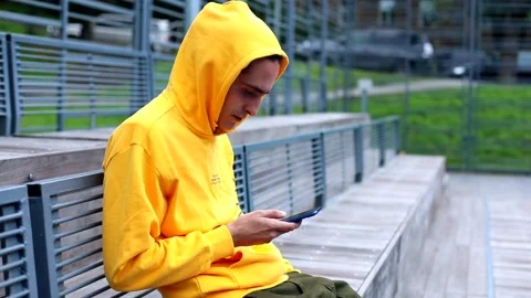 Young brunette man using smartphone outdoor on sports area in hoodie. Internet Video stock 135674843