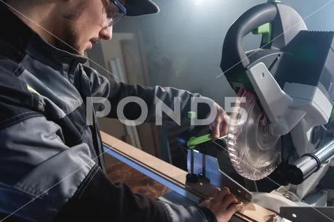 Young brunette man wearing a cap in a gray jacket by profession a carpenter cuts Stock Photos