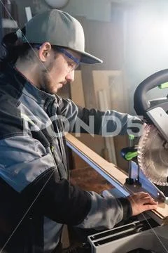 Young brunette man wearing a cap in a gray jacket by profession a carpenter cuts Stock Photos