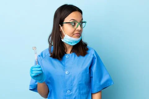Young brunette mixed race dentist woman holding tools over isolated backgroun Stock Photos