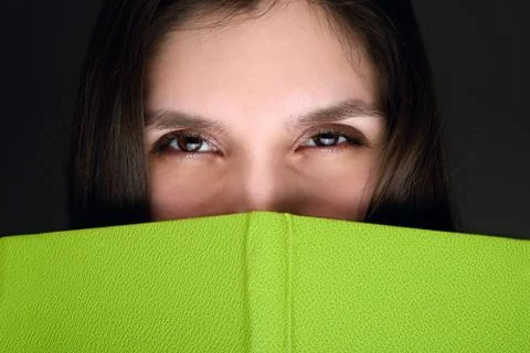 Young brunette model posing with green book covering half her face close-up Stock Photos