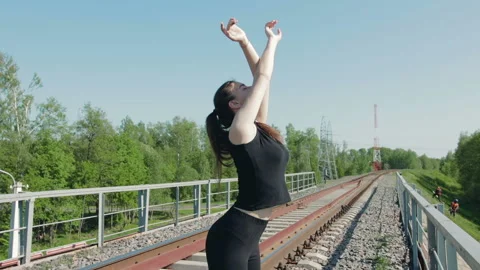 Young brunette performs breathing exercises on the railway bridge over the 動画素材 89853557