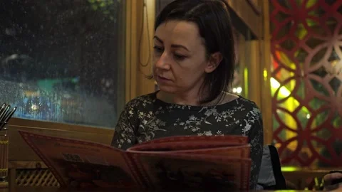 A young brunette is sitting at a table in a restaurant and choosing dishes from Stock Footage 170446337