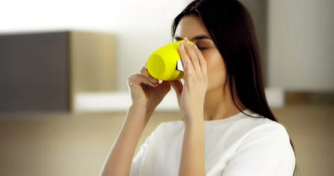 Young brunette standing in the kitchen and drinking a brewed tea bag from a mug. Stock Footage 176227405