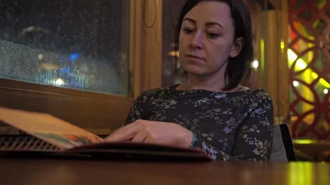A young brunette at a table in a restaurant flips through the dishes on the menu Stock Footage 170716597