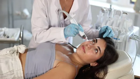 Young brunette undergoing device-driven facial treatment using ion bubble pen Stock Footage 331307532