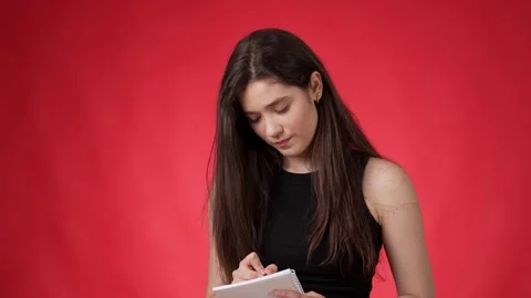 Young brunette writing in her notebook irritated against pink background Stock Footage 249524088