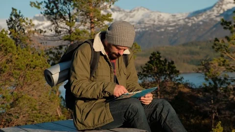 Young brutal man looking a map in a forest at sunset. Norway forest. Wooden Stock Footage 109370259