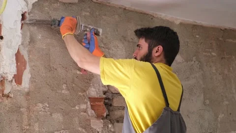 Young builder breaking up a house wall with a hammer and a chisel. Stock Footage 157694582