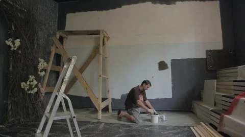 Young builder carefully mixes up gray paint in white plastic pail Stock Footage 66172051