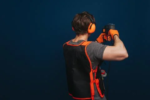 Young builder is drilling the wall, isolated over blue background Foto stock