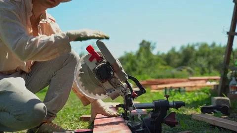 Young builder with glasses uses circular saw to cut wooden blanks. Building a Stock-Footage 266236444