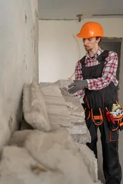 Young builder in hardhat collecting construction debris stones. House renov.. Stock Photos